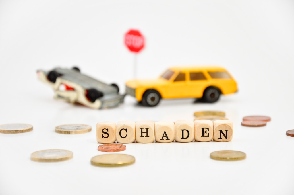 Unfall mit Spielzeugautos im Hintergrund, vorn Münzen und Würfel mit Buchstaben - Schaden