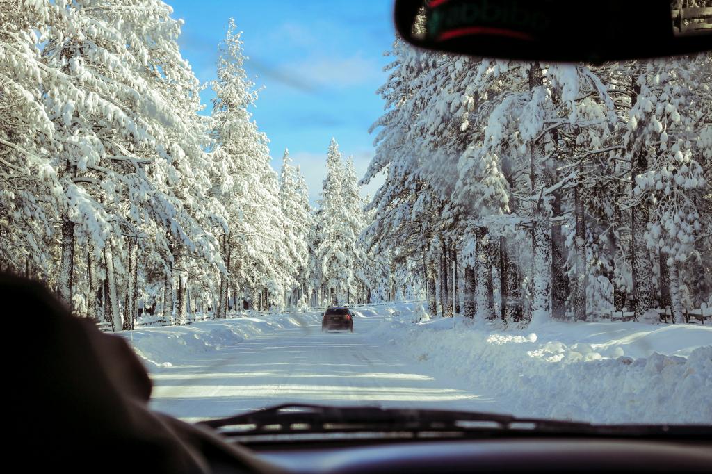 Blick aus dem Auto auf schneebedeckte Straße und Winterwald